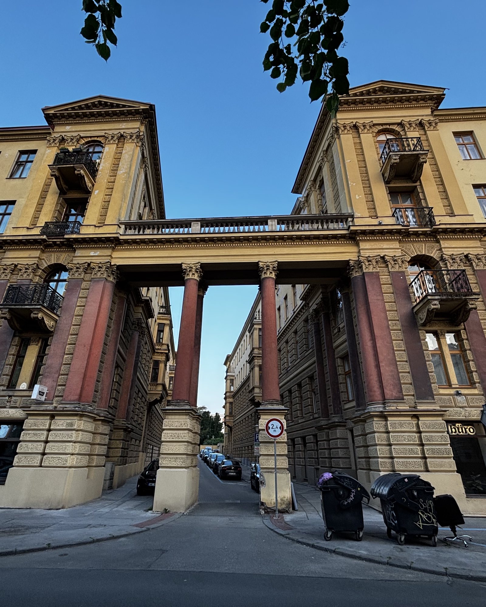 Büro 🤷‍♀️. Ornate balcanies, garbage bins, and old office chair, pillars, 2.4m Wide, grass, an open window with boxes of herbs and other flower pots. Marks on the render and a square sign.