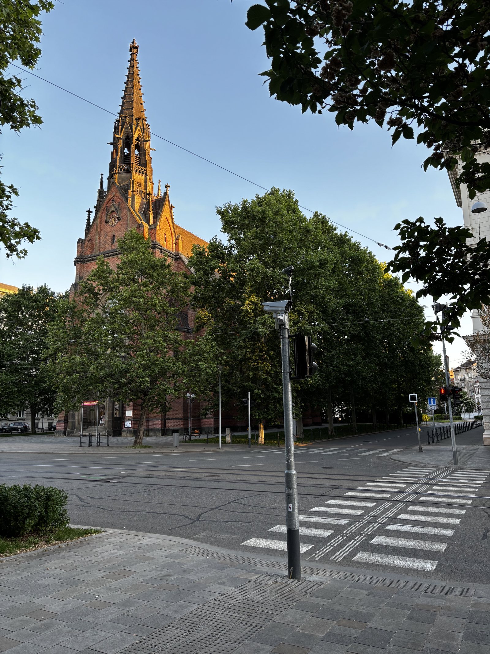 Českobratrský evangelický chrám Jana Amose Komenského. Security cameras, zap, pedestrian crossing, clock, catenary wires, tram tracks.